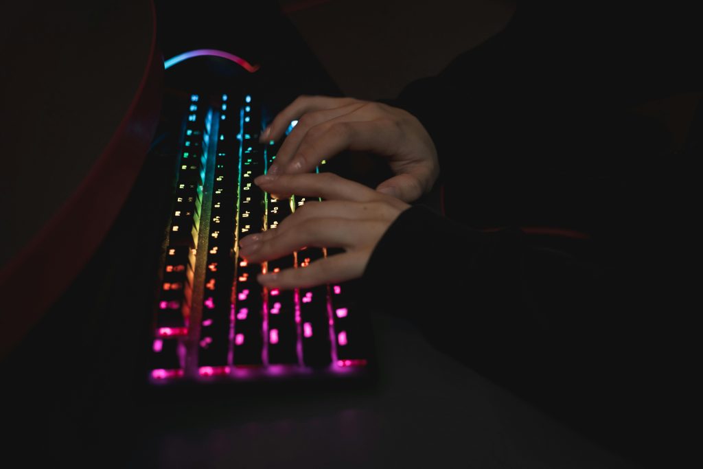 Close-up of hands typing on a colorful RGB backlit mechanical keyboard in a dimly lit environment.